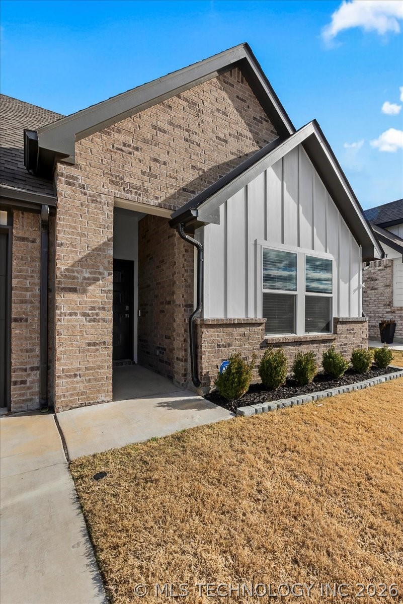Brick-and-siding home entrance with covered entry, front window, and landscaped walkway.