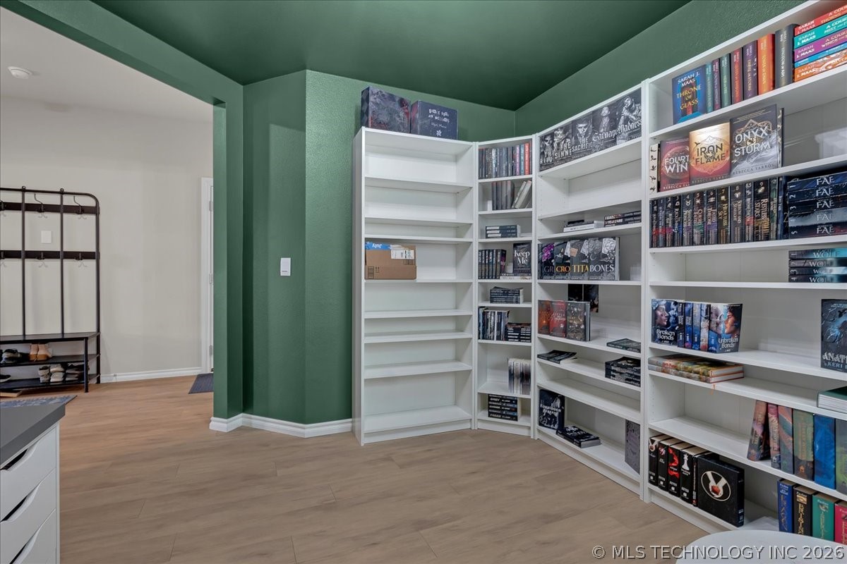 Home library with emerald-green walls, white built-in bookshelves, and wood-look flooring.