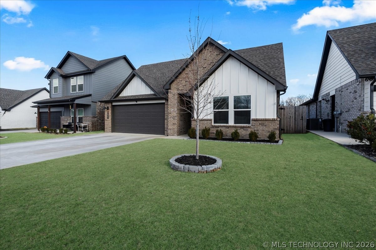 Single-story home with white siding, brick accents, a dark double garage door, and a broad green lawn.