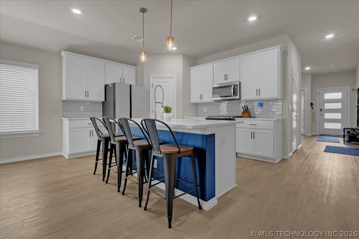 Kitchen with white cabinetry, stainless appliances, and a blue island with bar seating.