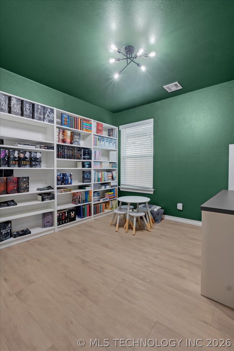 Home library with green walls, book-filled white shelves, and a small reading table.