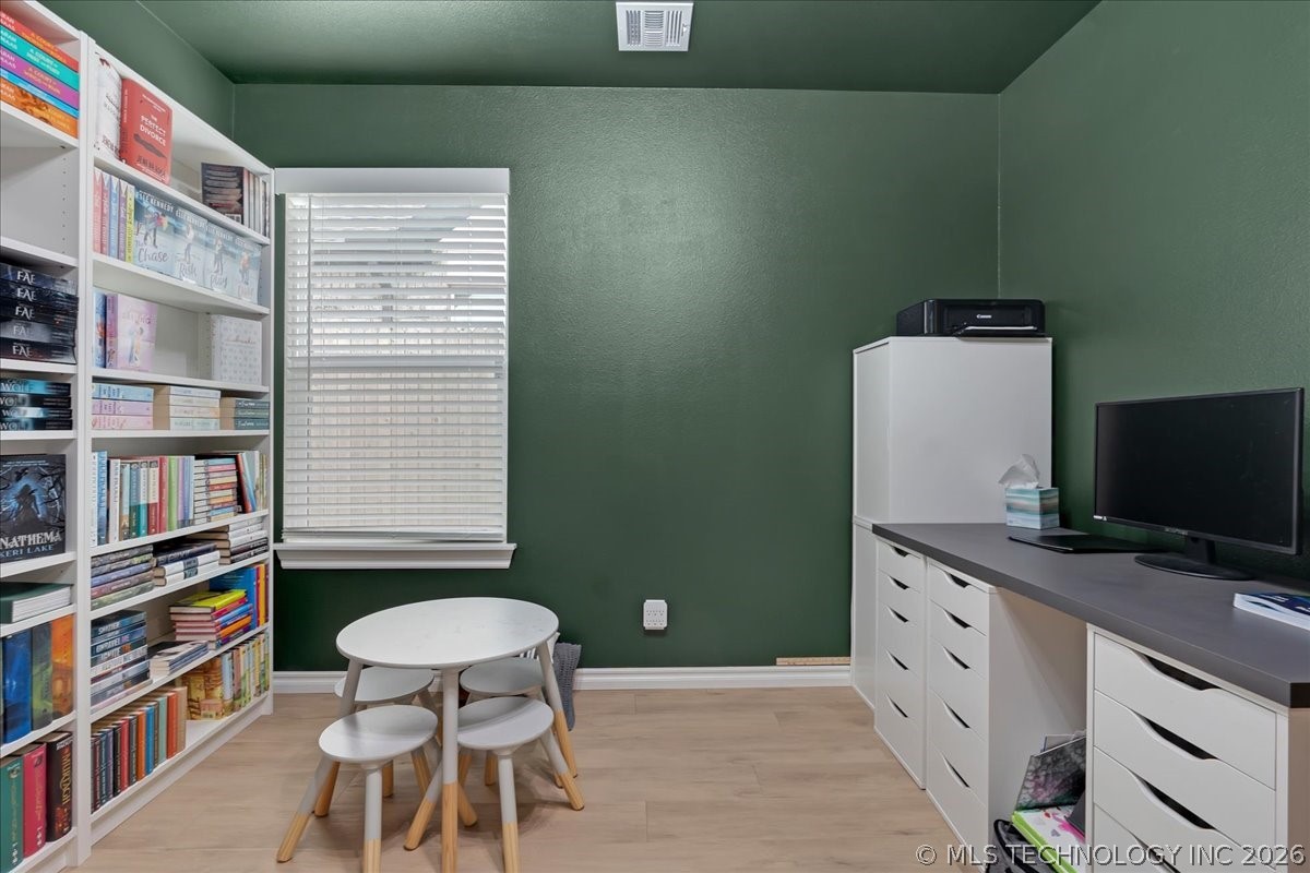 Office with green walls, book-filled shelves, white storage cabinets, and a small round table.
