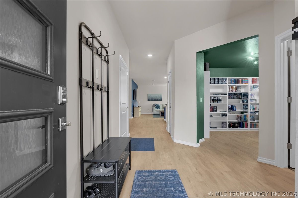 Entry hallway with a dark front door, coat rack and shoe bench, leading to a green-trimmed room with shelving.