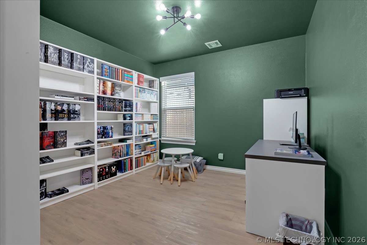 Home library with book-filled white shelves, green walls, and a desk with a computer.