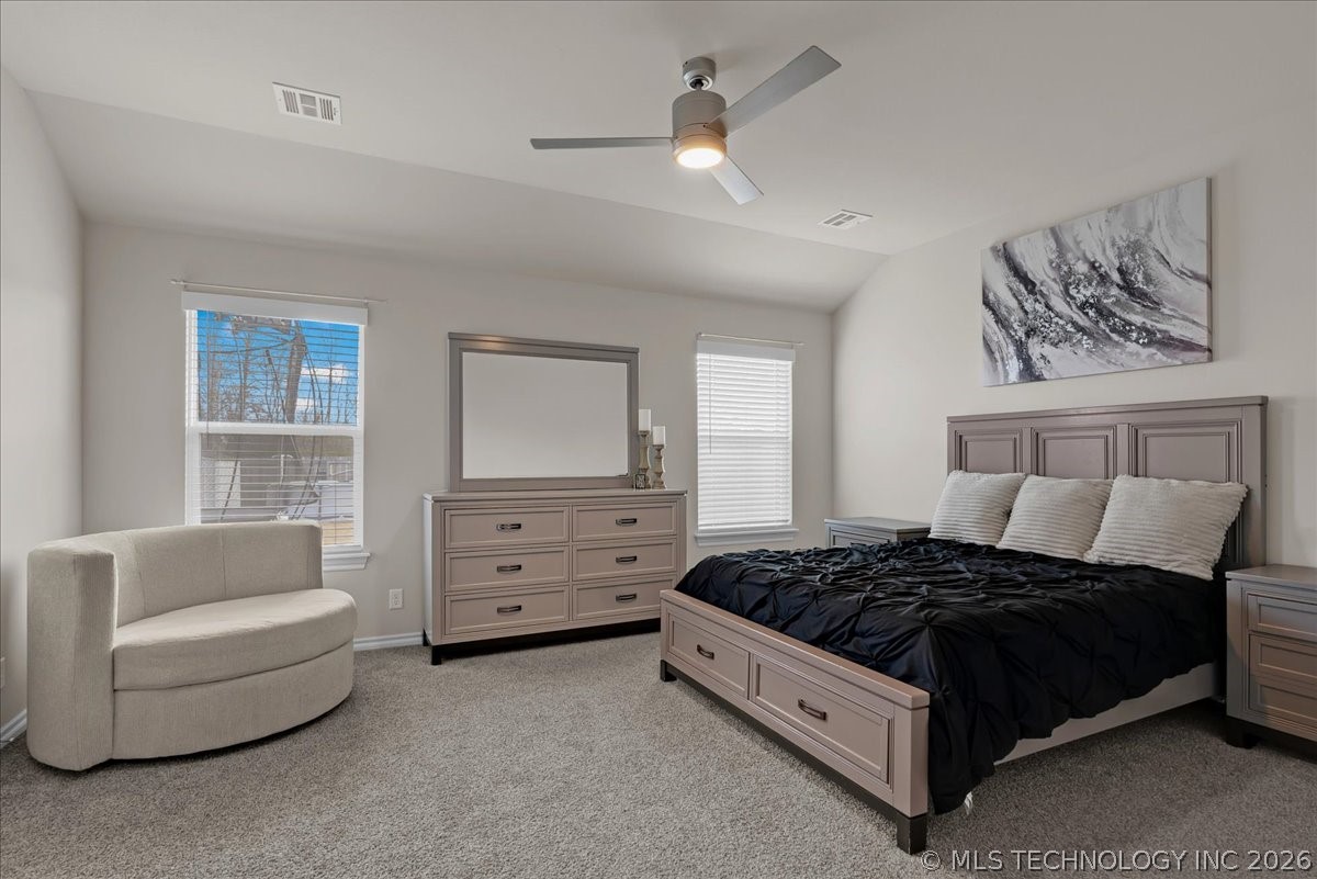 Furnished bedroom with a gray paneled bed, black bedding, and a curved upholstered chair.