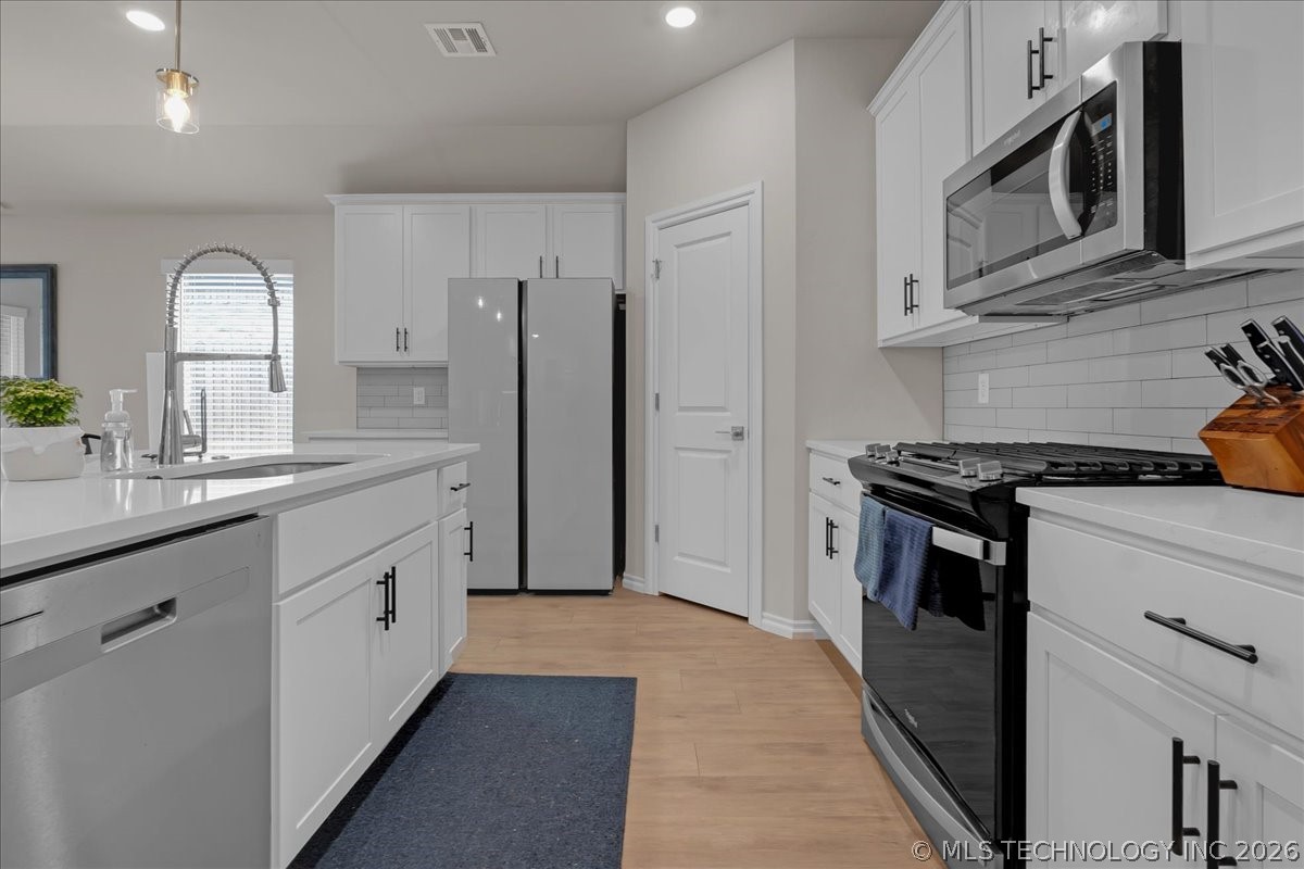 Kitchen with white cabinetry, stainless steel appliances, and a large island with sink.