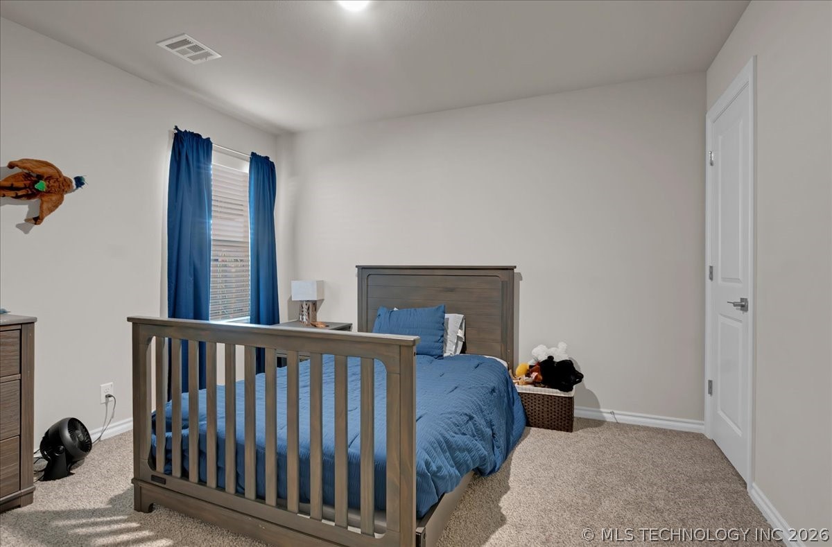 Bedroom with a blue bed, curtained window, and beige carpet.