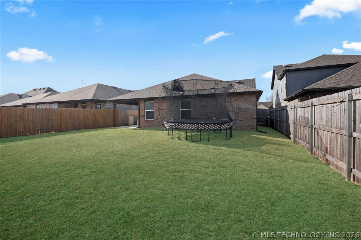 Fenced backyard with a broad green lawn, trampoline, and brick rear of the house.