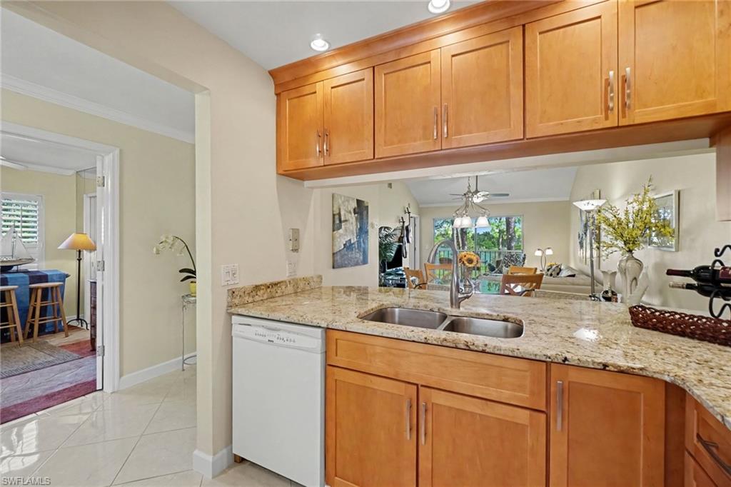 Kitchen with honey-colored cabinets, granite counters, a double sink, and an open view toward the living area.