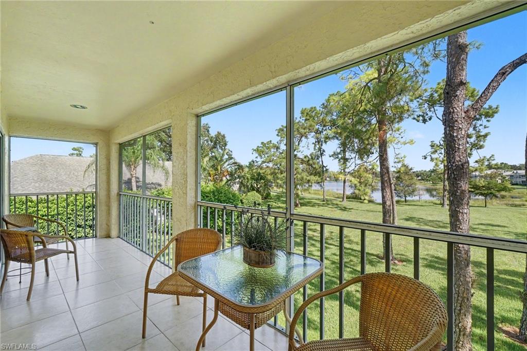 Furnished balcony overlooking a lake and grassy grounds, with wicker seating and mature trees.