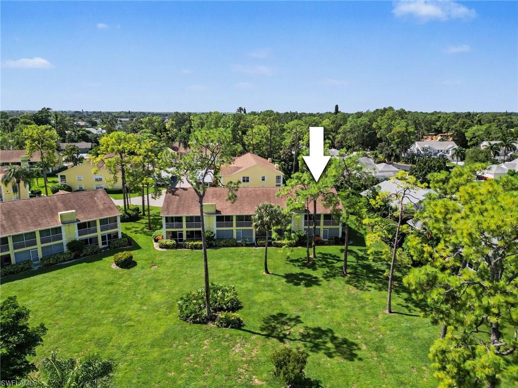 Aerial view of condominium buildings and landscaped grounds, with a white arrow marking a unit.