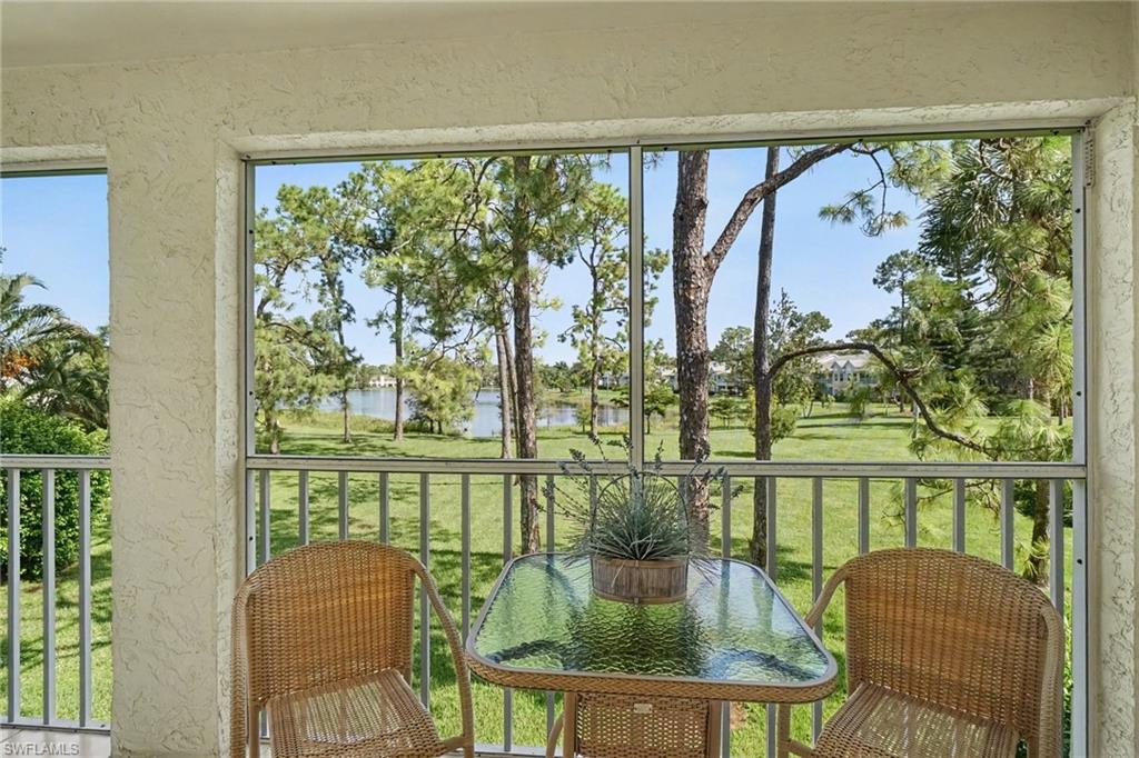 Screened balcony with wicker chairs and a glass-top table overlooking a lawn and lake.