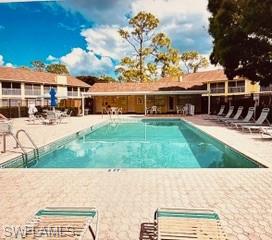 Outdoor swimming pool bordered by lounge chairs and low-rise apartment buildings.