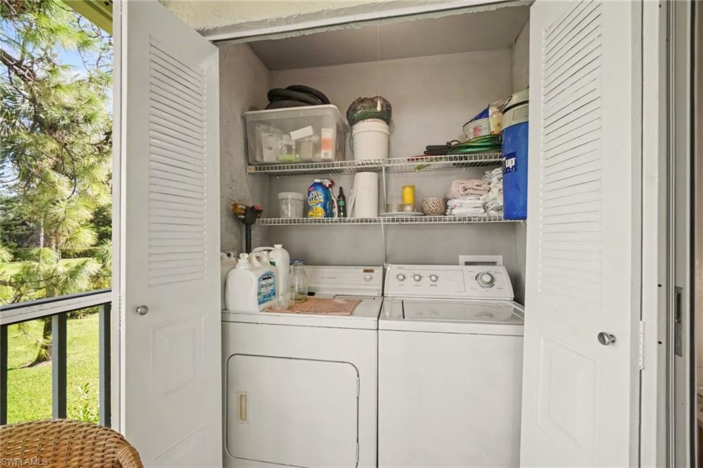 Laundry closet with washer and dryer, stocked wire shelves, and open doors to a tree-lined balcony.