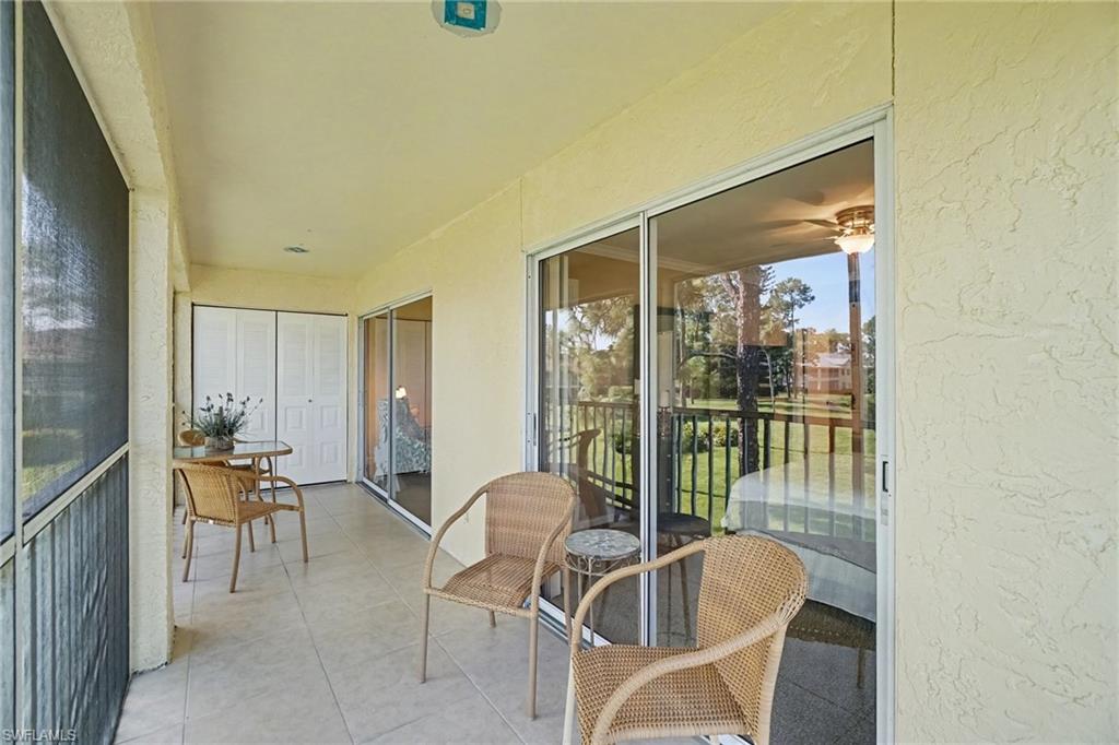 Screened condo lanai with wicker seating overlooking a grassy area and trees.