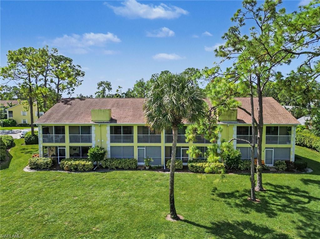 Two-story green condominium building with white-railed balconies, framed by palm trees and a broad lawn.