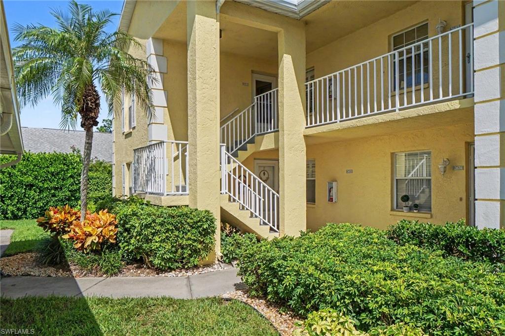 Yellow stucco residential building with white-railed exterior stairs, balconies, and tropical landscaping.