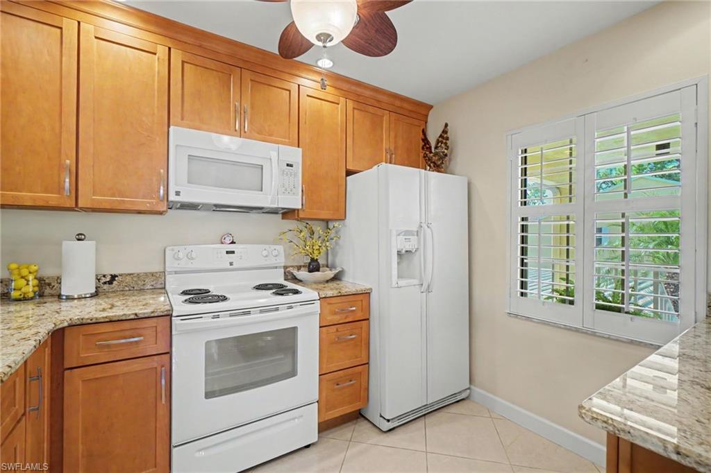 Kitchen with wood cabinets, granite counters, white appliances, and a plantation-shuttered window.
