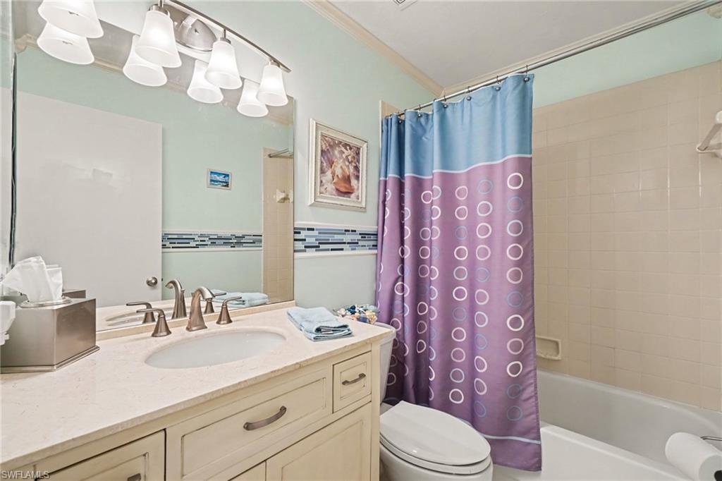 Bathroom with a cream vanity, large mirror, and bathtub behind a blue and purple patterned curtain.