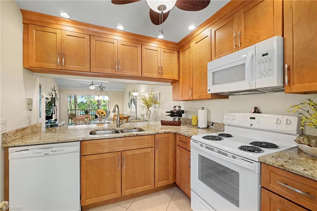 Kitchen with honey-colored cabinets, granite counters, white appliances, and an open view into the dining area.