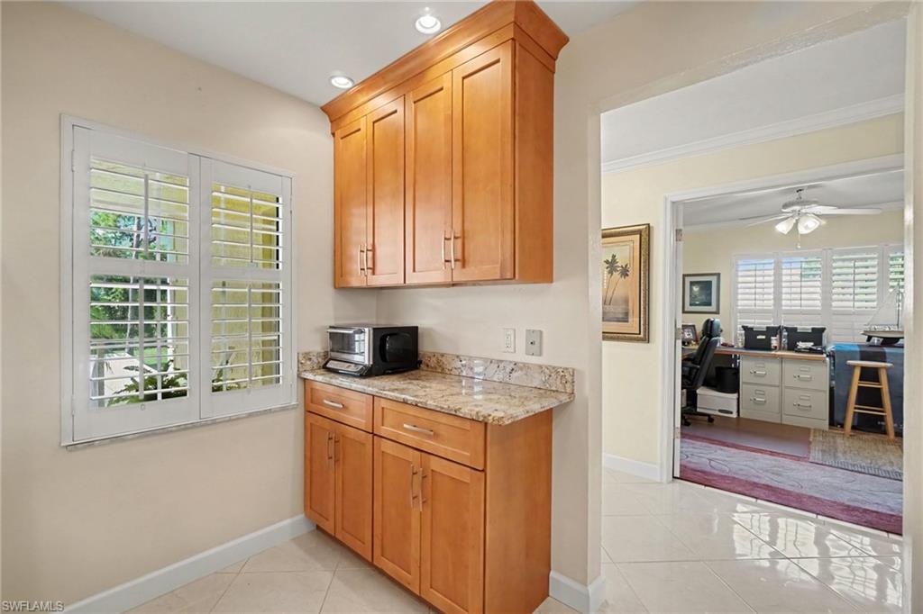 Built-in wood cabinets and stone counter beside a plantation-shuttered window, opening to an office.