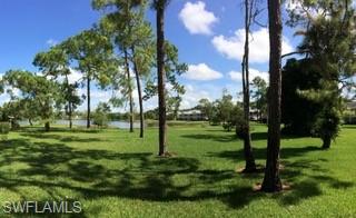 Landscaped lawn with tall trees and a pond in the distance.
