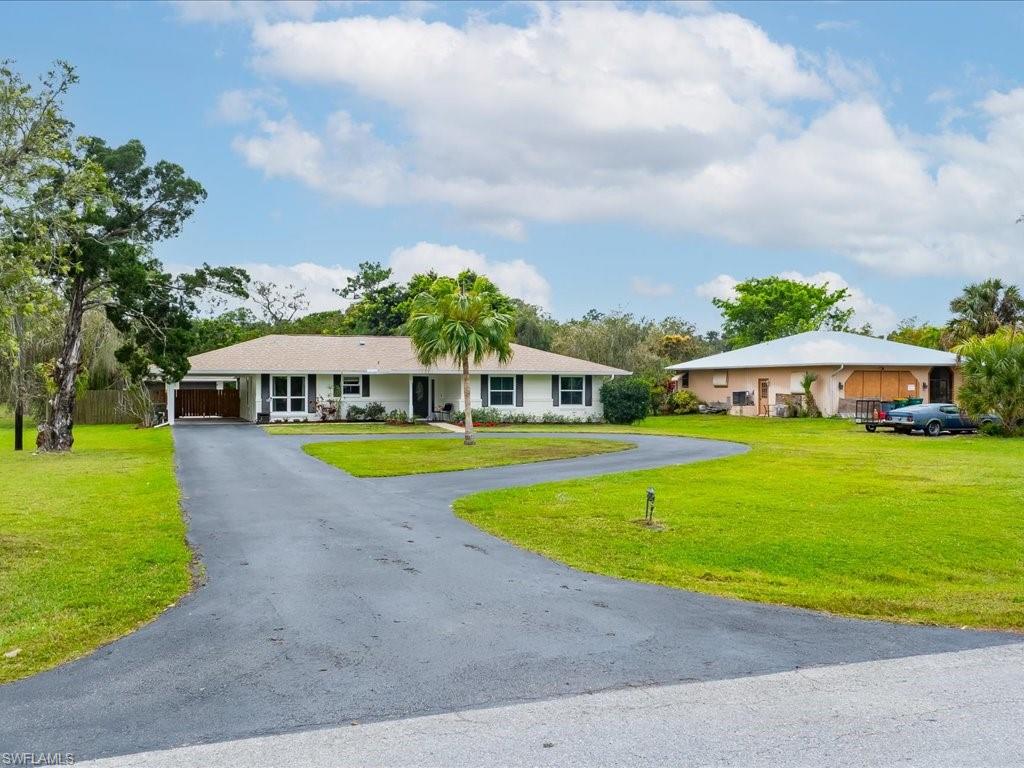 Single-story home with a circular driveway, broad lawn, and palm tree.