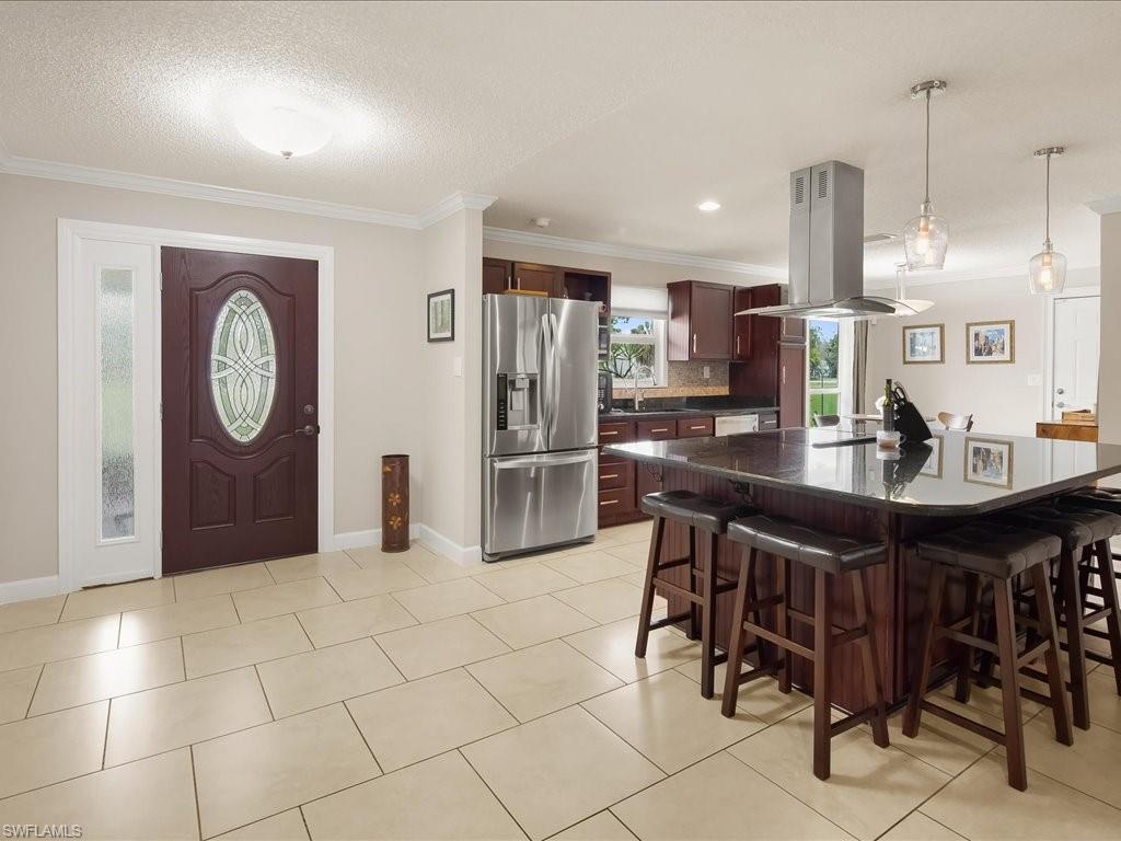 Open kitchen with dark wood cabinets, stainless steel appliances, and a large island with bar stools.