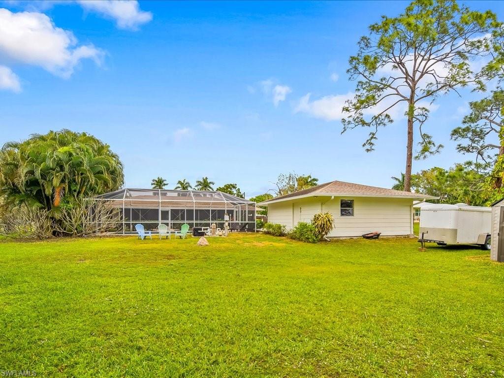 Backyard of 5272 Myrtle Lane with a screened pool enclosure, lawn, mature trees, and a white trailer.