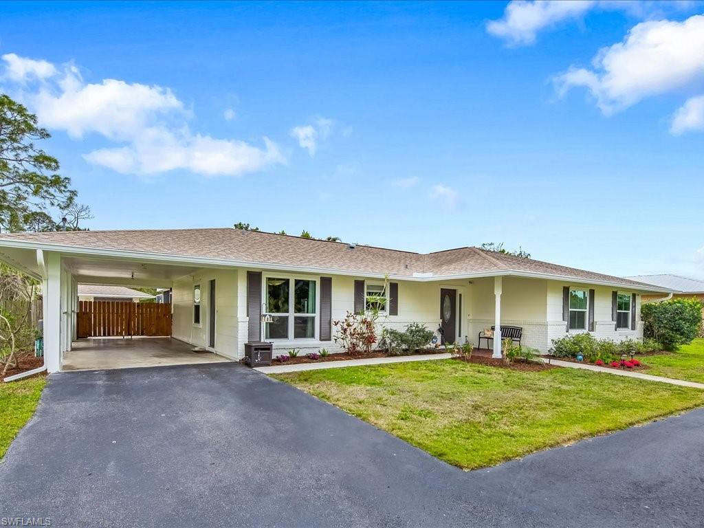 Single-story white house with a carport, dark shutters, and a broad paved driveway.