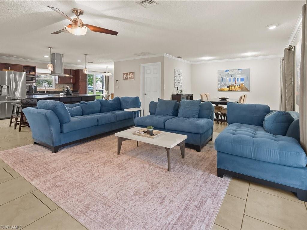 Open-plan living room with blue sofas, a pale rug, and an adjoining kitchen and dining area.