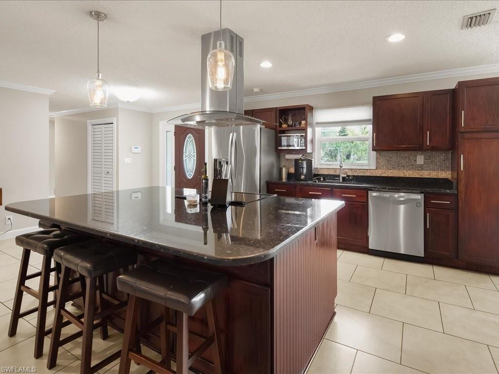 Kitchen with a granite island, dark cherry cabinetry, stainless steel appliances, and bar stools.
