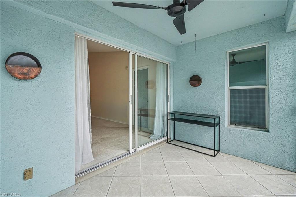 Tiled lanai with blue stucco walls, a ceiling fan, and sliding glass doors opening to an empty room.