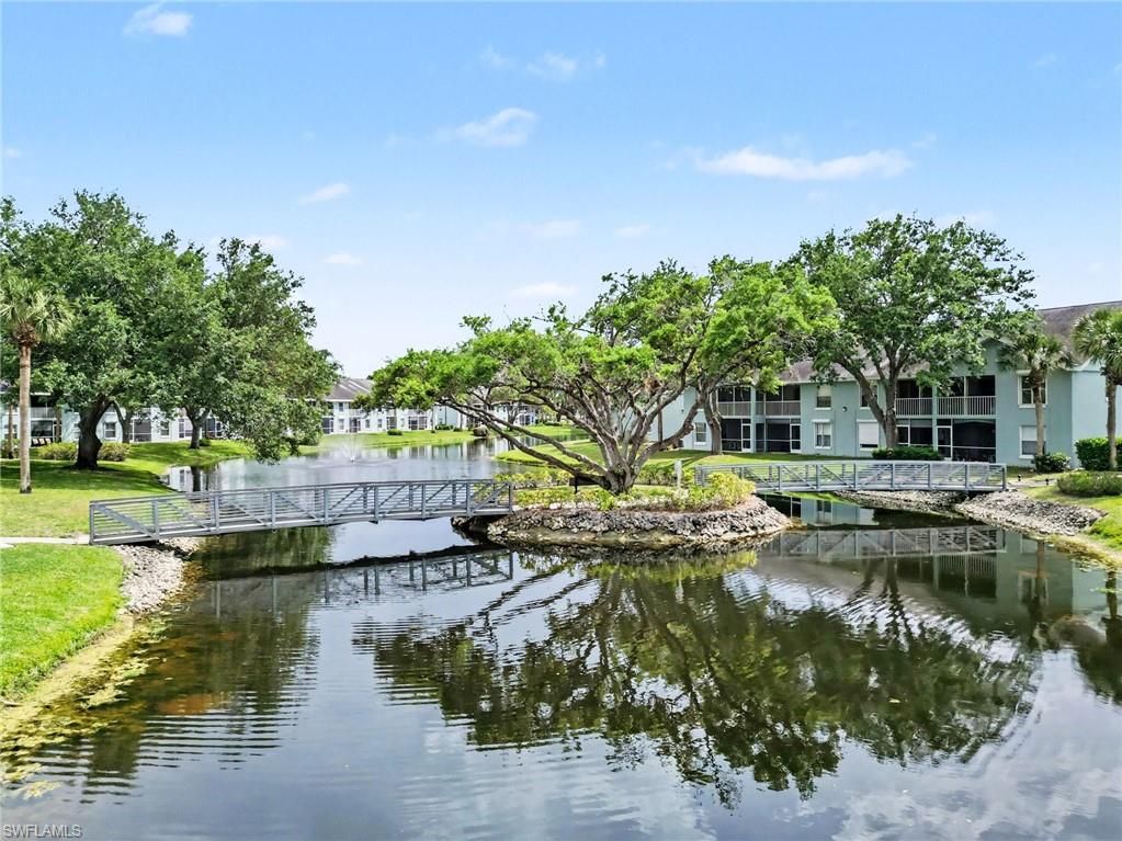 Condominium buildings beside a pond, with a pedestrian bridge and tree-covered island.