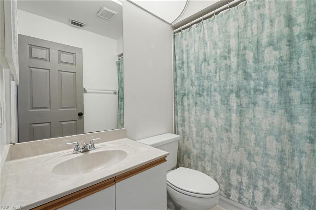 Bathroom with a white sink vanity, toilet, and teal patterned shower curtain.