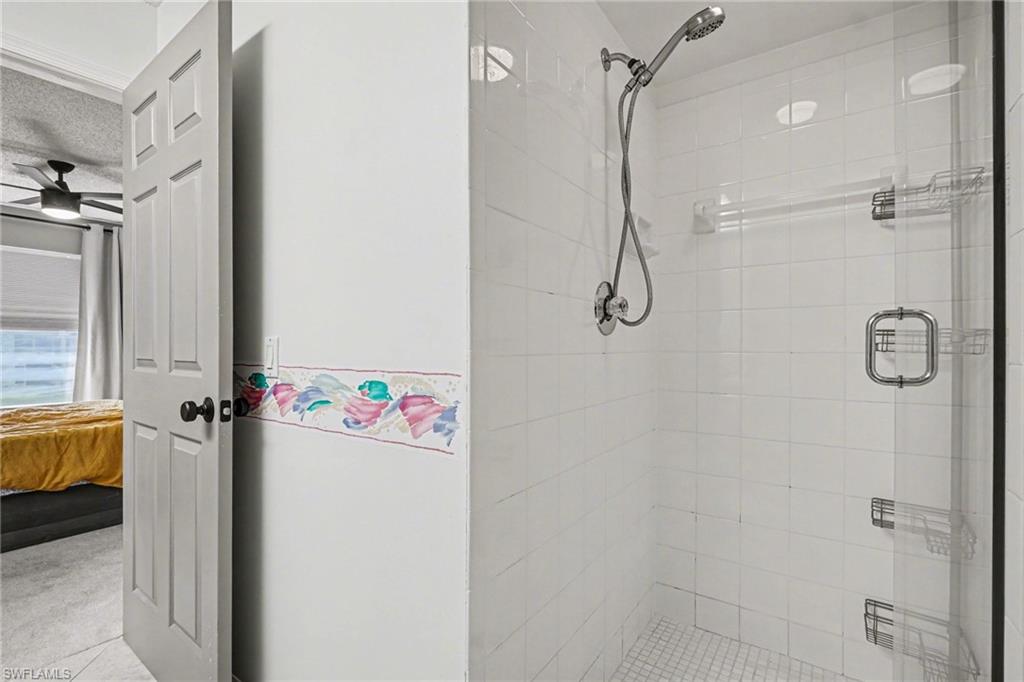 White tiled walk-in shower with chrome shelving and a colorful border beside an open bedroom door.