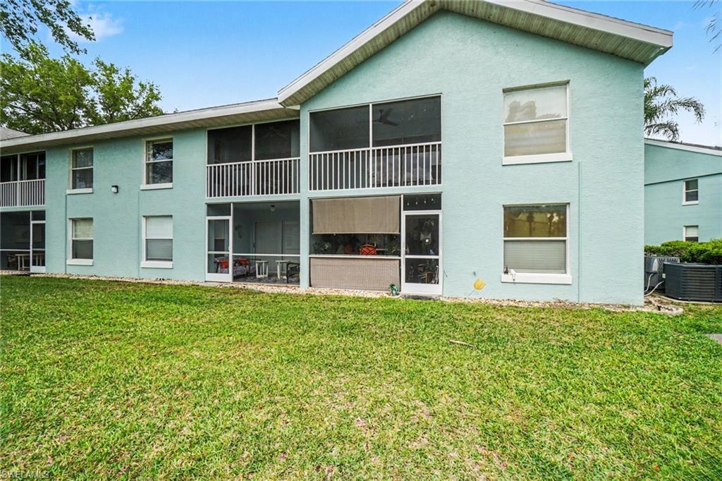 Pale aqua two-story condominium exterior with screened balconies and a broad green lawn.