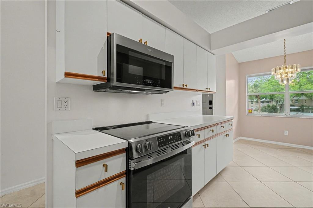 Kitchen with white cabinets, stainless steel range, and an adjoining dining area with a chandelier.