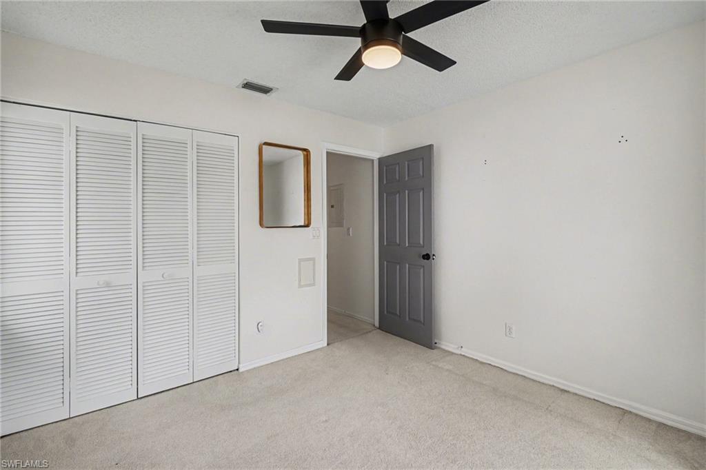 Empty carpeted bedroom with louvered closet doors and a dark ceiling fan.