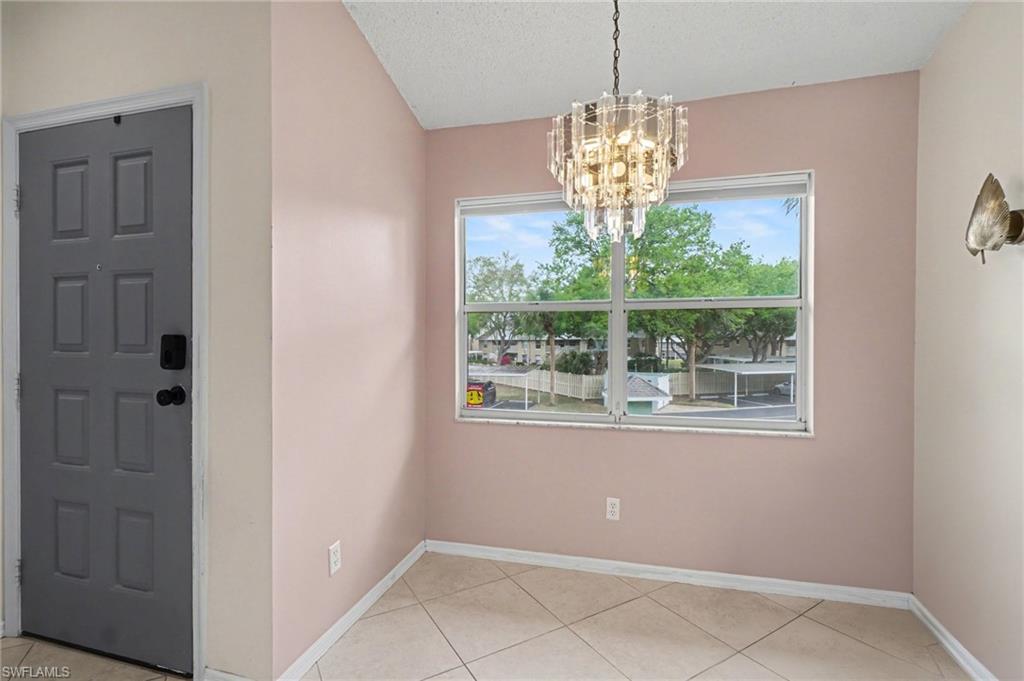 Empty dining area with a crystal chandelier, tiled floor, and large window overlooking trees.