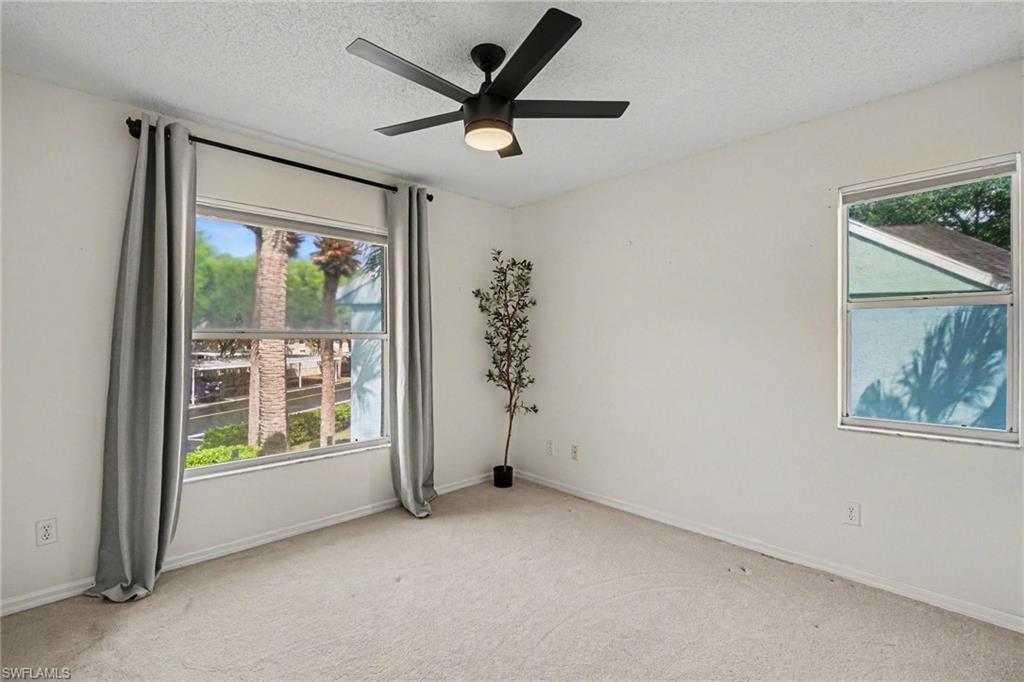 Vacant bedroom with gray curtains, a black ceiling fan, and palm trees visible through the windows.