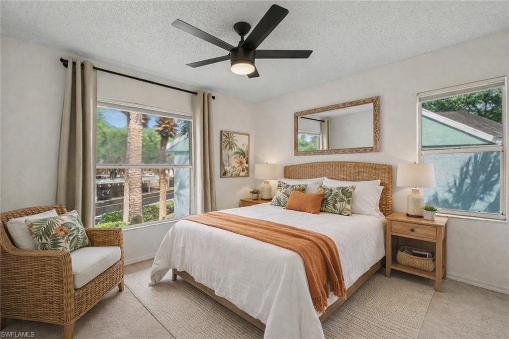 Bedroom with a wicker headboard, white bedding, rust-colored throw, and a wicker armchair by the window.
