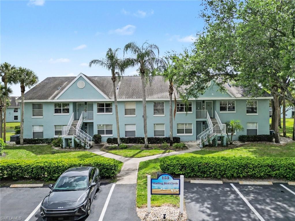 Light blue two-story condominium building with white staircases, palm trees, and a Wading Bird Circle sign.