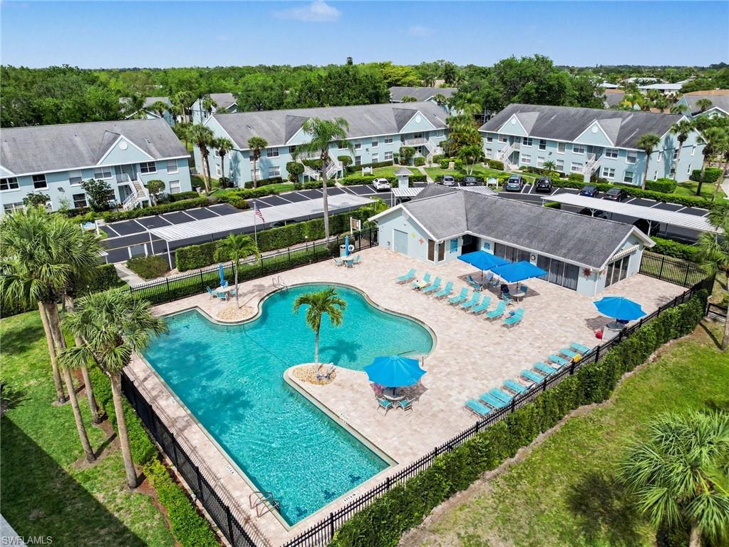 Aerial view of a community pool with blue umbrellas, surrounded by residential buildings.