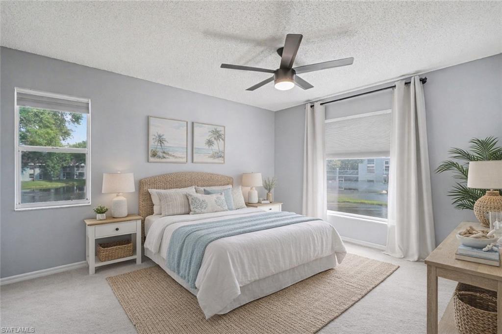 Staged bedroom with a king-size bed, woven headboard, pale blue throw, and windows overlooking water.