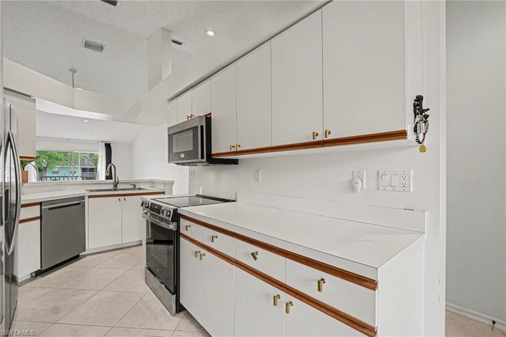 Kitchen with white cabinets, wood trim, stainless appliances, and a window overlooking greenery.