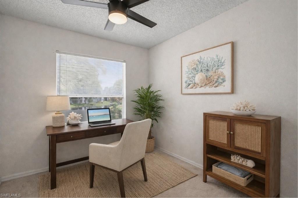 Staged home office with a desk by the window, upholstered chair, potted palm, and cane-front cabinet.