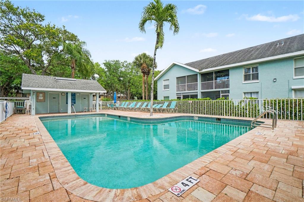 Community pool with a brick paver deck and light blue condominium building.