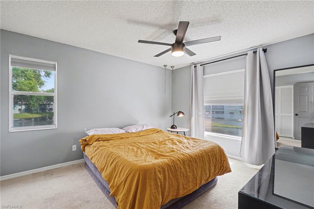 Bedroom with mustard bedspread, ceiling fan, and windows overlooking water and greenery.