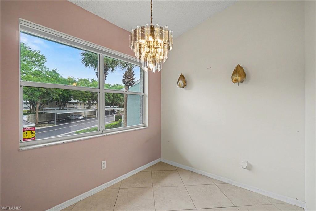 Unfurnished dining area with a crystal chandelier, tiled floor, and large window overlooking trees and parking.
